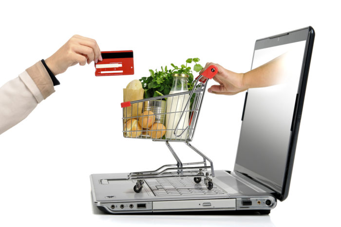 Hand with credit card and a small shopping cart coming from  laptop screen isolated in white